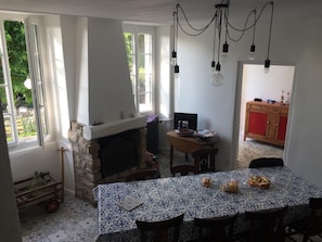 A dining area with a patterned tablecloth, a fireplace, and a view of the outdoors through large windows.