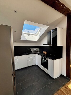 A modern kitchen with a skylight, white cabinets, black countertops, and a built-in oven.