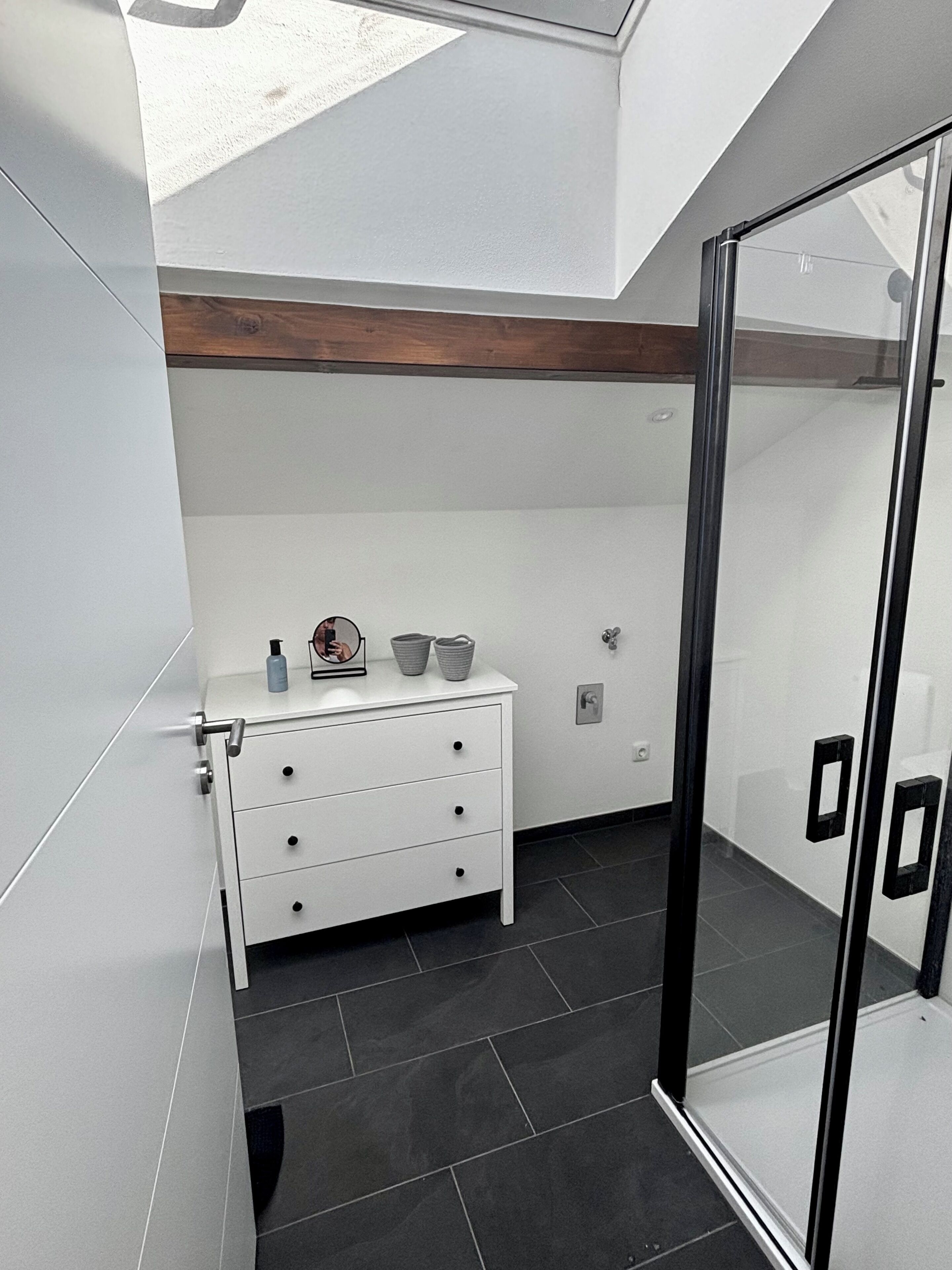 Une salle de bain moderne avec une douche à parois de verre, un meuble-lavabo blanc doté de tiroirs et un plafond avec poutres en bois.
