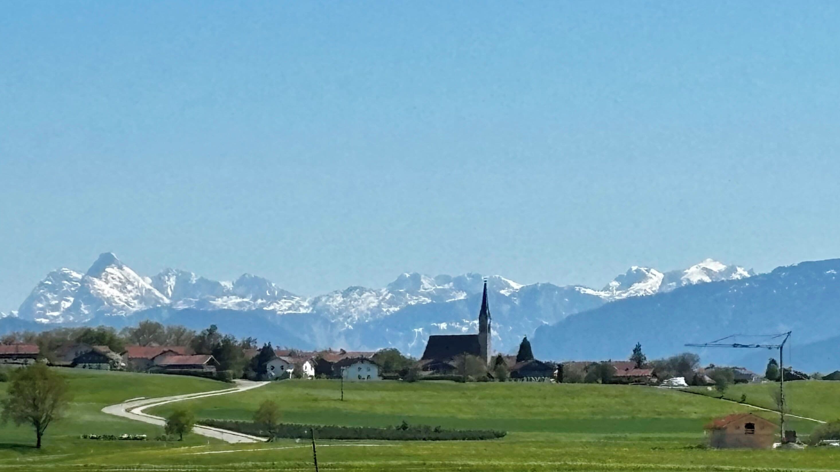 Ländliche Landschaft mit einer Kirche, Häusern und schneebedeckten Bergen im Hintergrund.