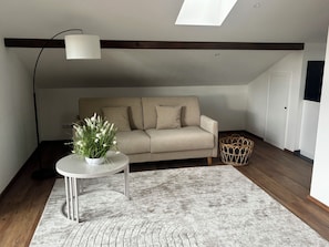 A living room with a sofa, a small table with a plant, a floor lamp, and a woven basket. - Vacation at the enchanting “Oberstübchen” above the rooftops of Traunstein (Traunstein)