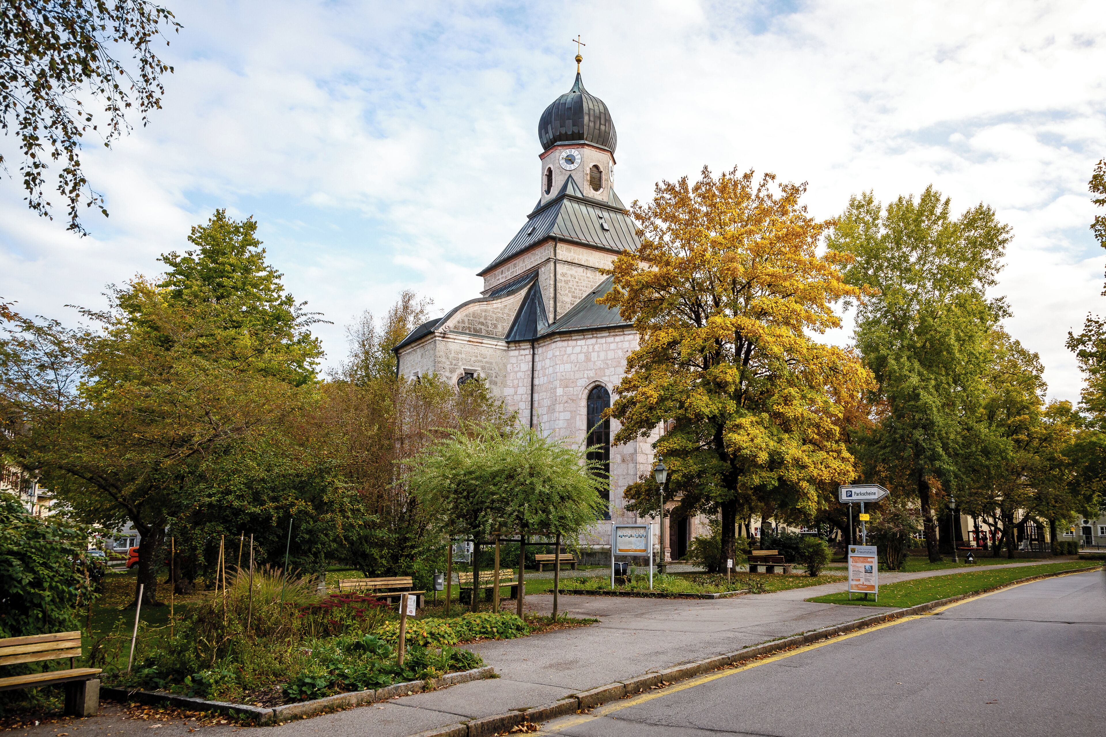 A church with a bell tower and a clock, surrounded by trees and benches.