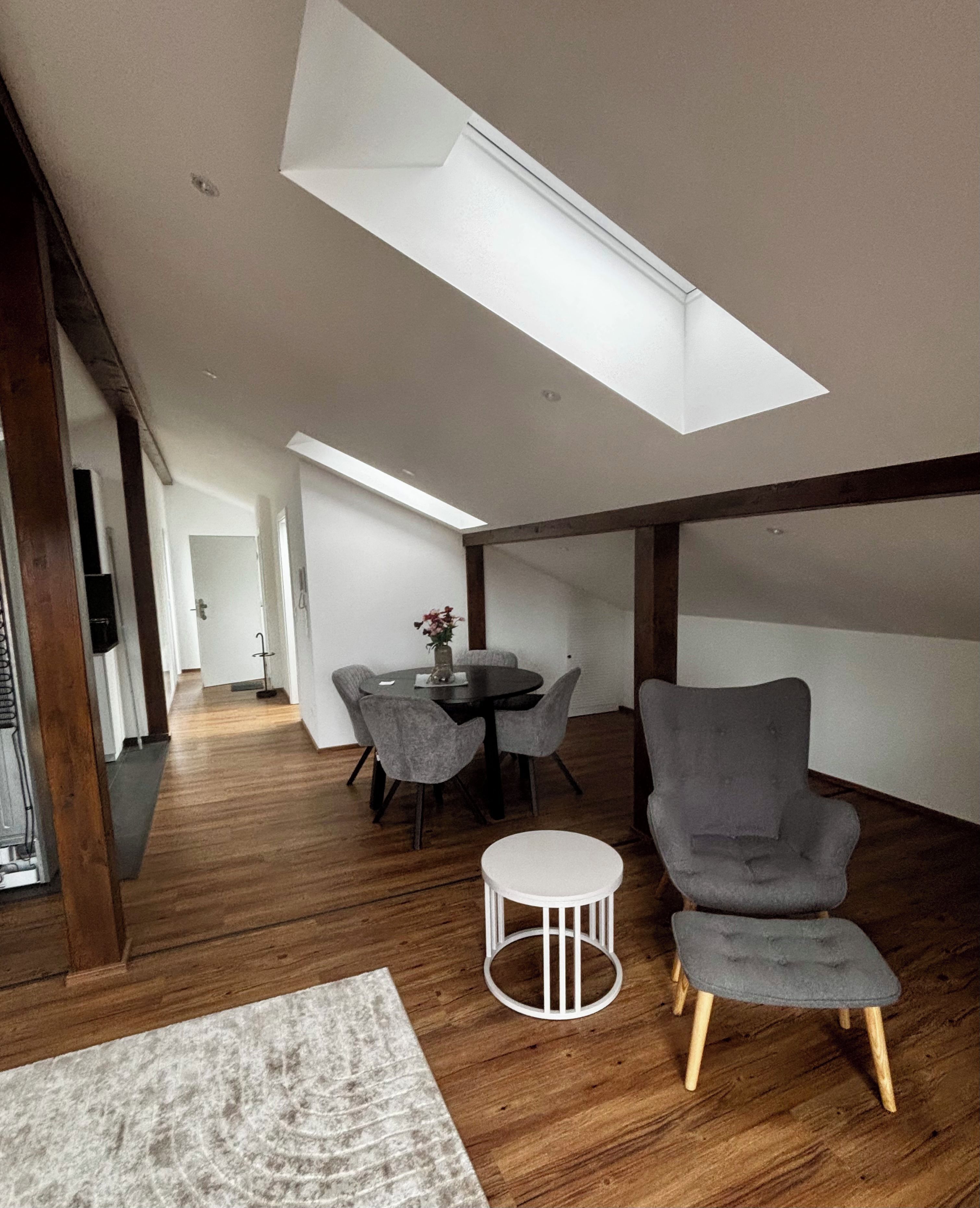 Een modern interieur met dakraam, houten vloer en grijze gestoffeerde stoelen.