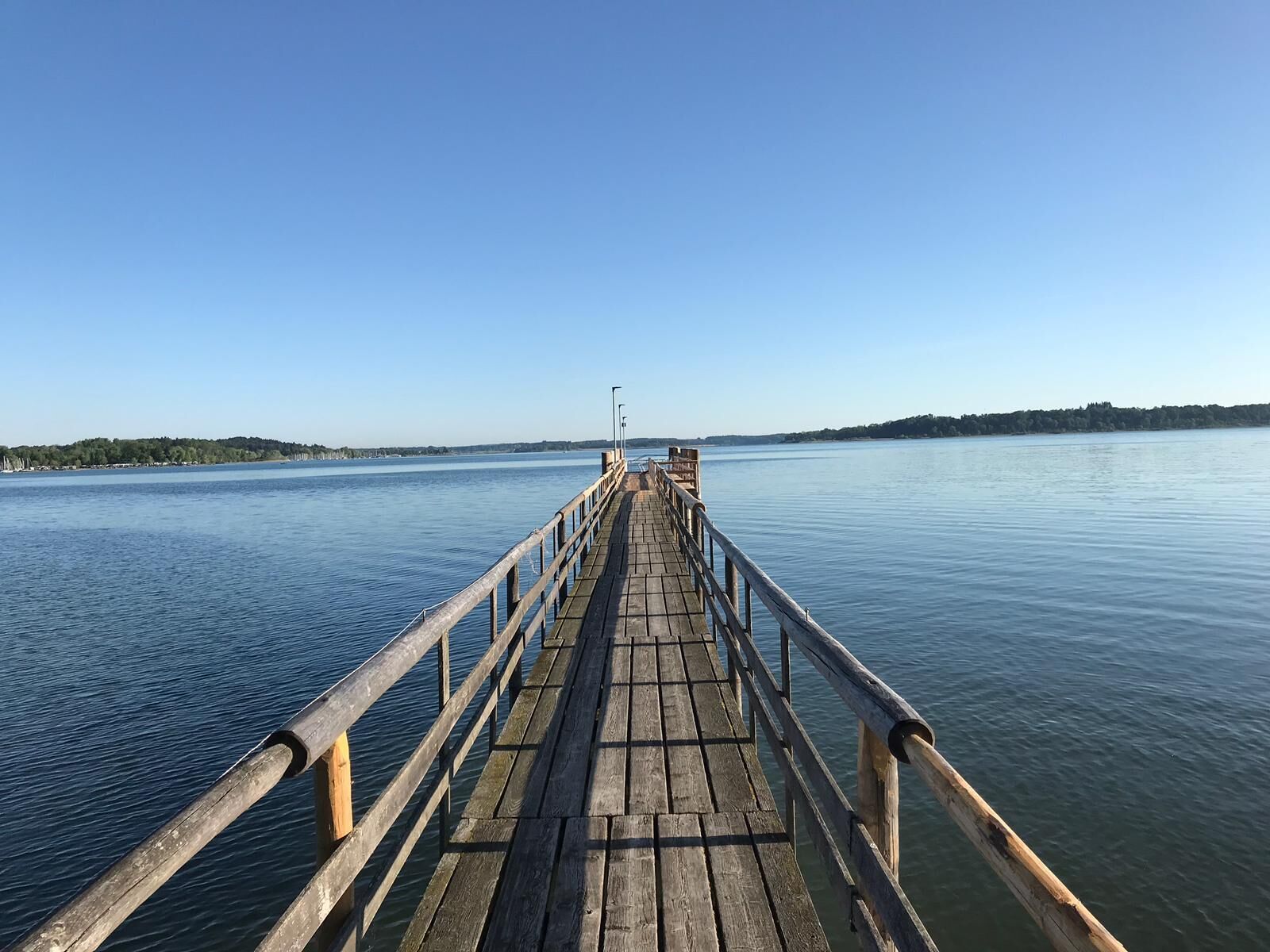 A wooden pier extending into calm water with a clear sky above.