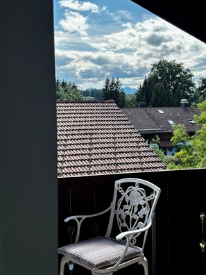 A balcony with a view of a residential area, a wooden fence, and a white metal chair.