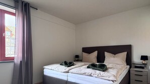 Un dormitorio con una cama, una mesita de noche, una lámpara y un ventanal con cortinas.