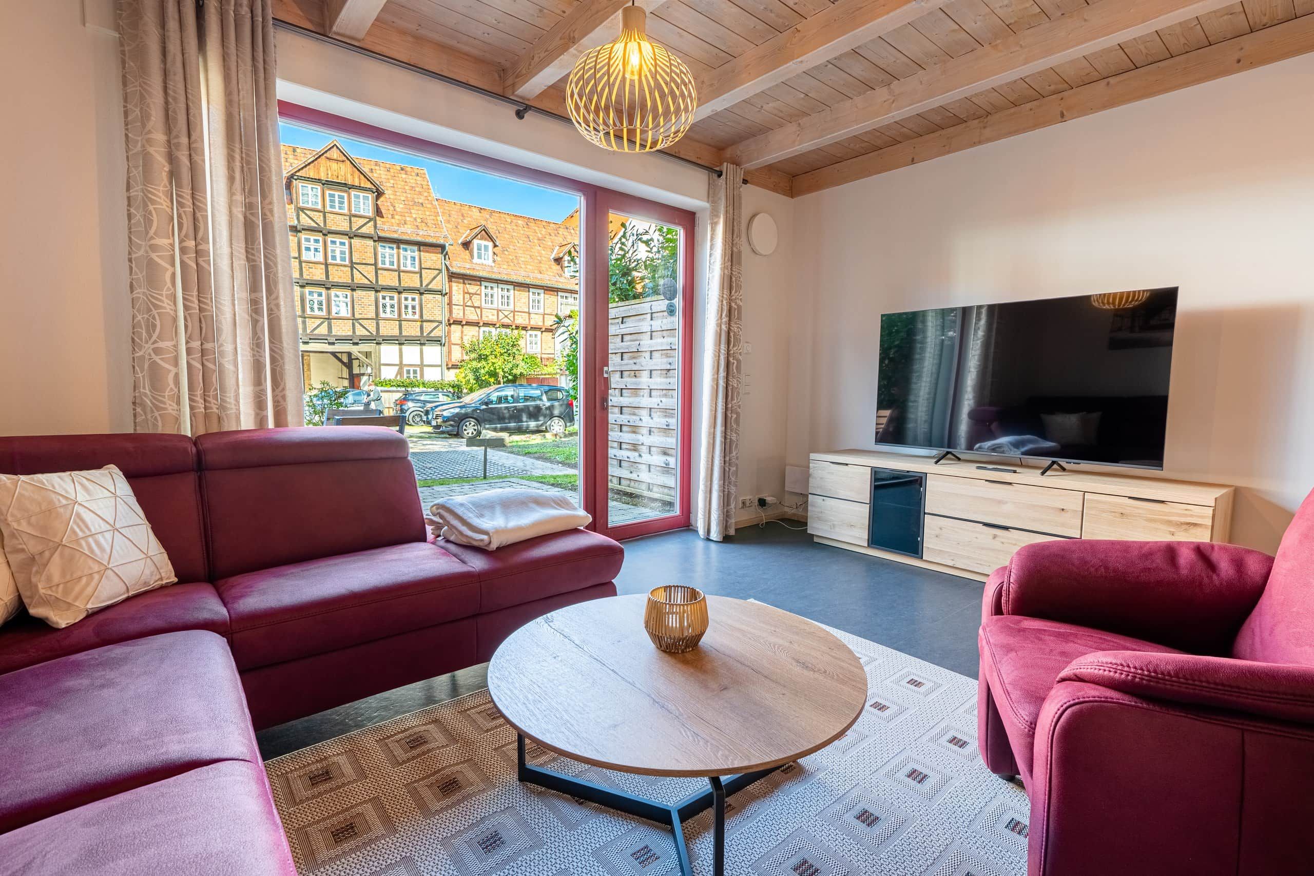 Un salon moderne avec un canapé rouge, une table basse ronde et un téléviseur posé sur un meuble en bois.
