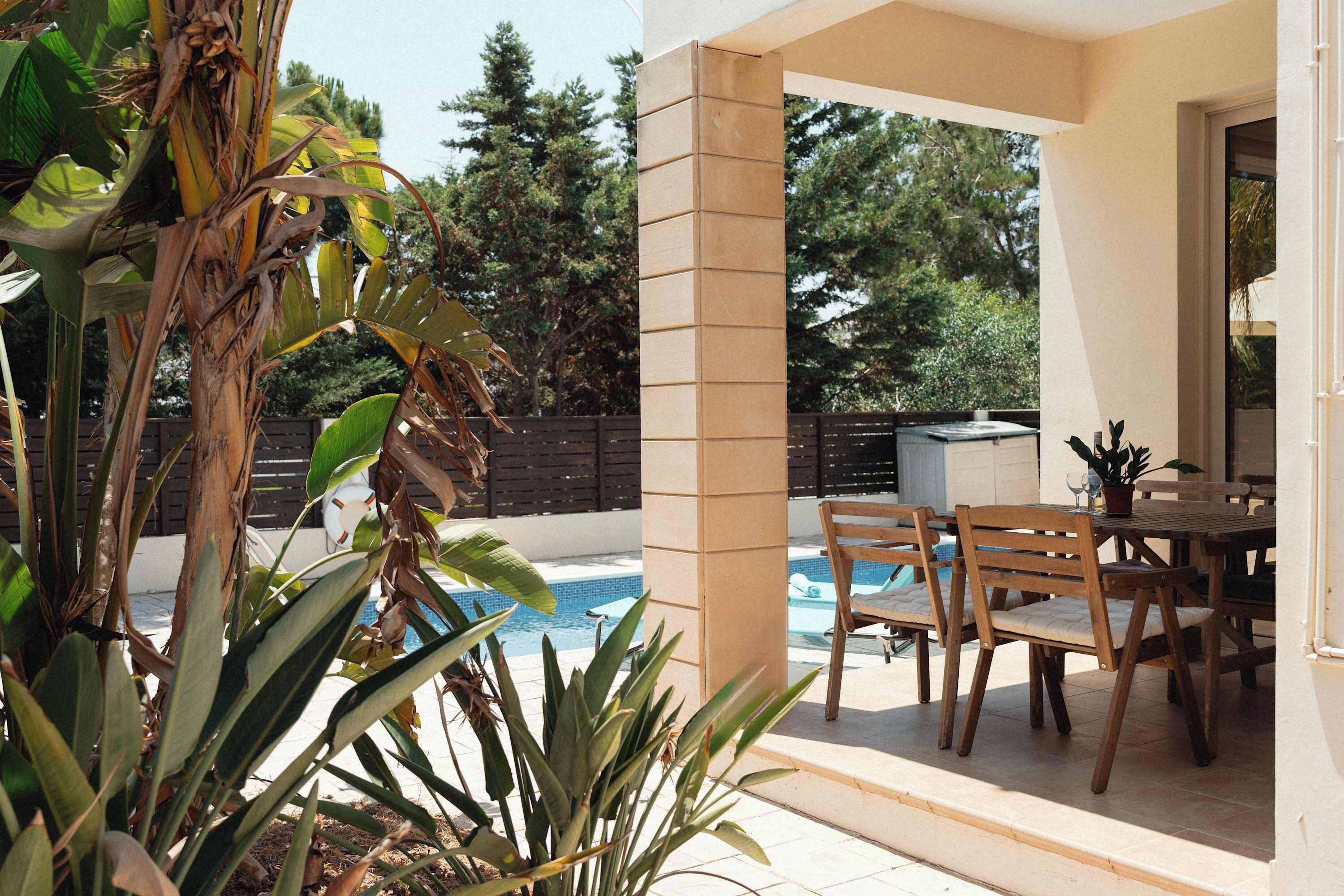 An outdoor patio area with a pool, wooden furniture, and tropical plants.