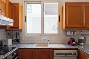 Eine moderne Küche mit Holzschränken, einem Backofen, einem Geschirrspüler und einem Fenster mit Blick nach außen.