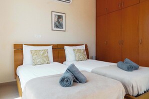 A hotel room with two beds, each with a white bedspread and a patterned pillow, and a wooden wardrobe. - 2BR Villa with Private Pool Near Fig Tree Bay (Paralimni)