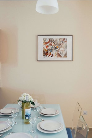 Ein Essbereich mit einem Tisch für vier Personen, einem gerahmten abstrakten Gemälde an der Wand und einem klaren Kunststoffstuhl.
