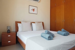 Een opgemaakt bed met witte lakens en twee opgerolde handdoeken, een nachtkastje met een lamp, en een kledingkast met schuifdeuren.