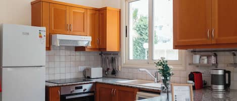 Una cocina con armarios de madera, un refrigerador blanco, un tostador, una cafetera y una ventana con vistas a árboles.