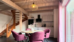 A modern kitchen with a dining area, featuring a staircase, a pendant light, and a large window. - Elementa City Lodge Quedlinburg 2 (Quedlinburg)