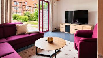 Ein modernes Wohnzimmer mit Holzbalkendecke, einem großen Fernseher und einer Sofagarnitur.