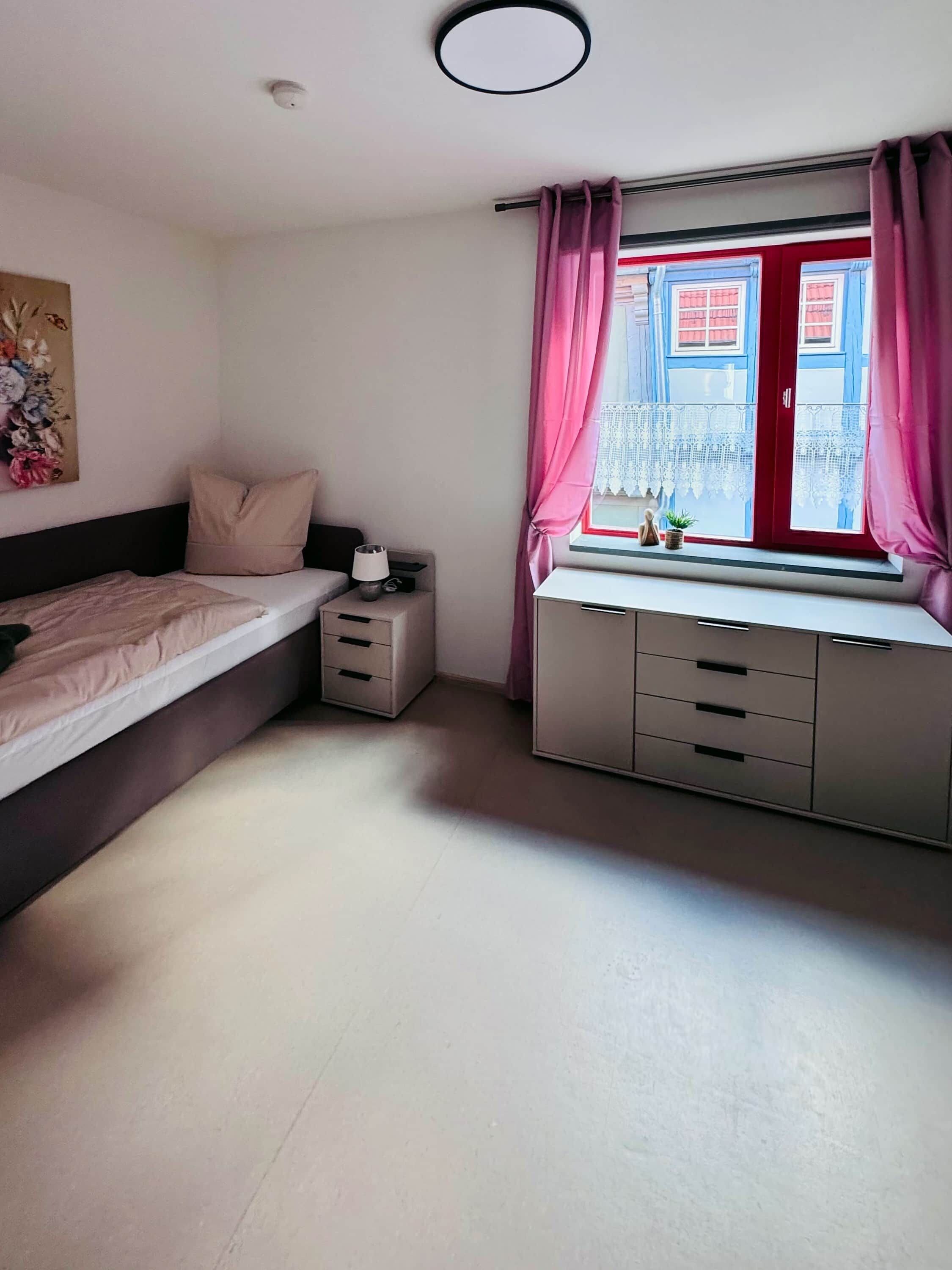 A bedroom with a bed, bedside table, lamp, and a window with curtains.