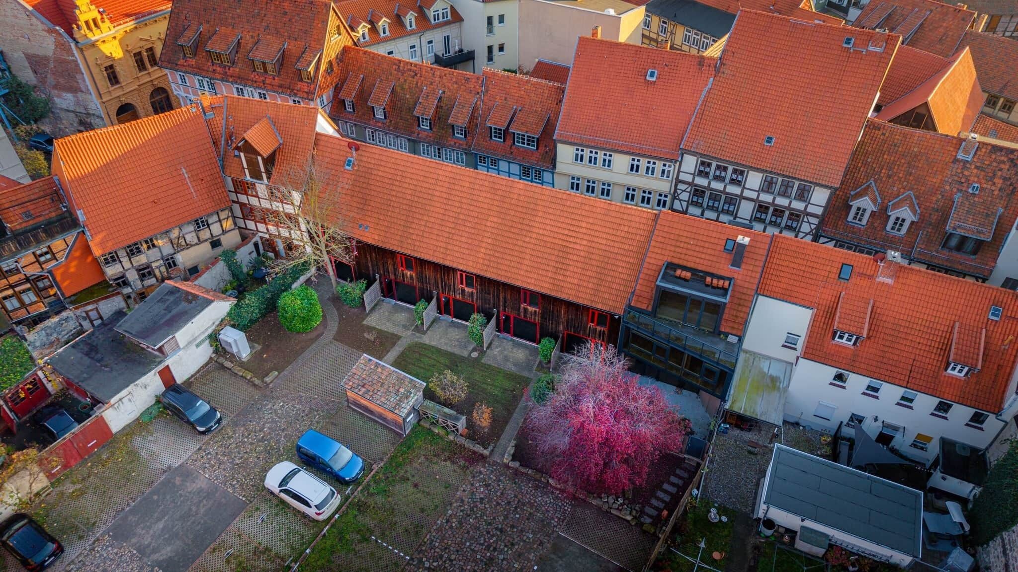 Oversigtsbillede af et boligområde med røde tegltage, en blanding af traditionel og moderne arkitektur, samt en lille parkeringsplads med biler.