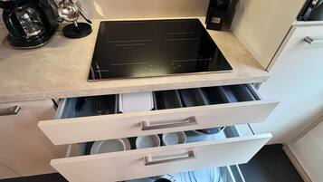 A kitchen with a black induction cooktop, a coffee maker, and a set of utensils.