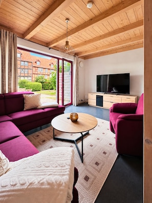 A modern living room with a wooden ceiling, a large TV, a sofa, and a coffee table. - Elementa City Lodge Quedlinburg 4 (Quedlinburg)