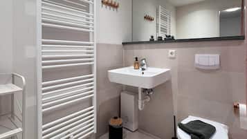 Un baño moderno con lavamanos, espejo y retrete blancos. Hay un perchero y un pequeño cubo de basura.