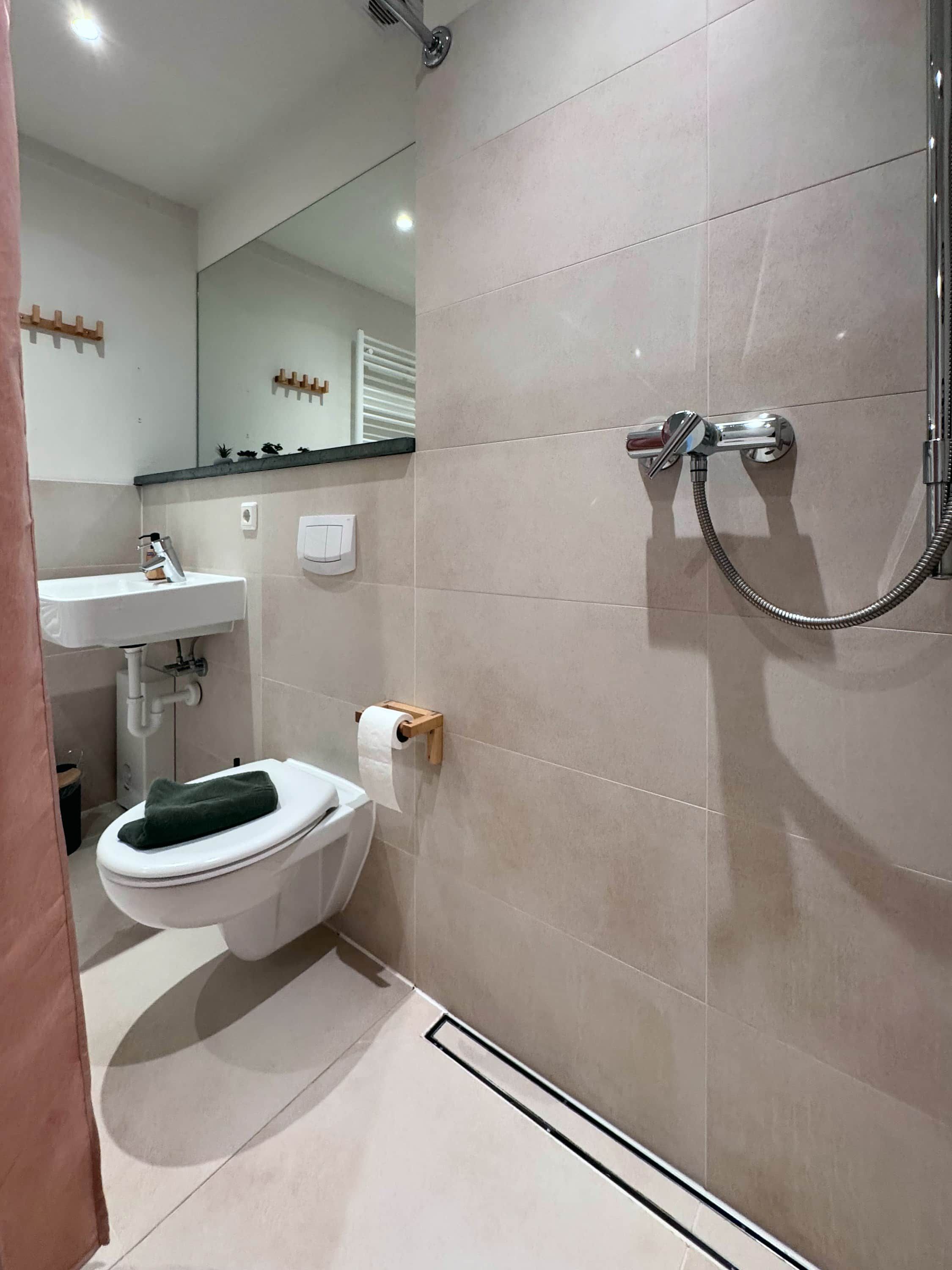 Badeværelse med toilet, håndvask, spejl og bruser.