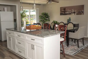 Una cocina con una isla grande, armarios blancos y un comedor con mesa y sillas.