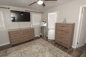Un dormitorio con dos cómodas de madera, un ventilador de techo, un televisor de pantalla plana y un espejo grande.