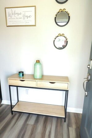 Quarto com mesa de console de madeira, um vaso verde e duas espelhos na parede.