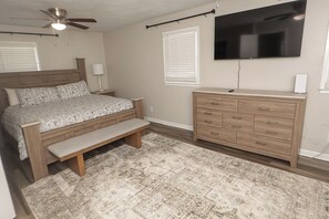 Un dormitorio con cama, banco, cómoda, televisor y ventilador de techo.