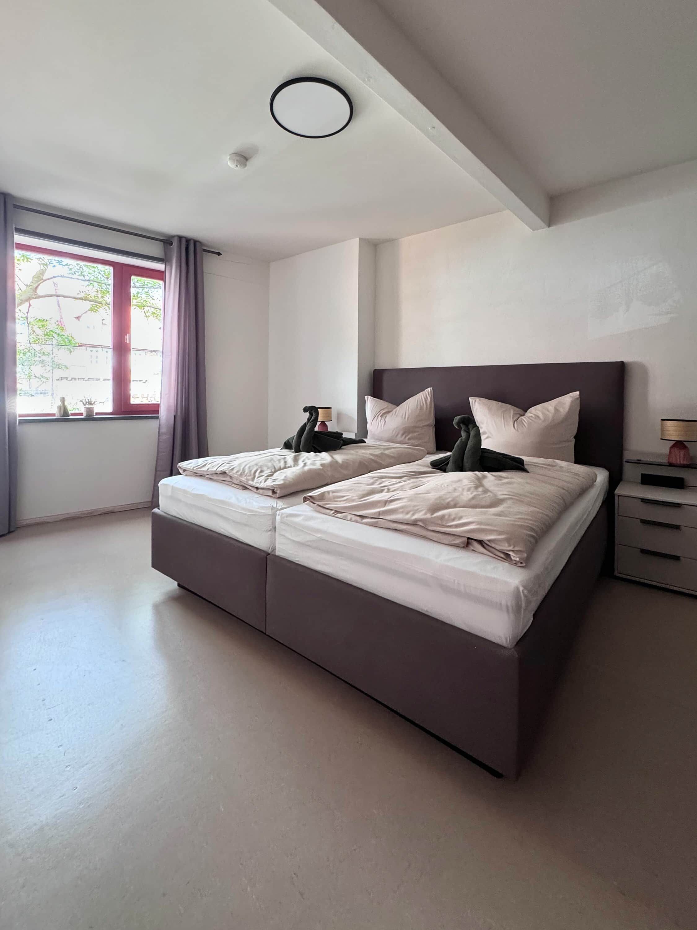 Une chambre à coucher moderne avec un grand lit, une table de chevet, une lampe et une fenêtre avec des rideaux.