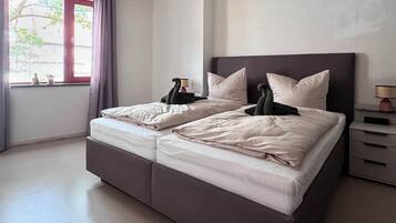 Une chambre à coucher moderne avec un grand lit, une table de chevet, une lampe et une fenêtre avec des rideaux.