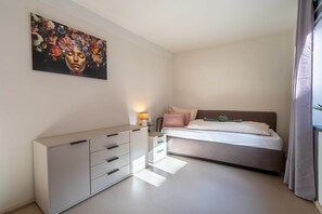 A bedroom with a bed, a bedside table, a lamp, a dresser, and a painting on the wall.