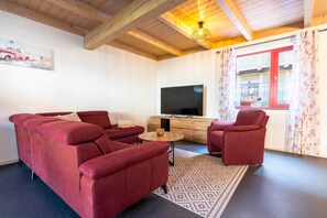 A living room with a sectional sofa, a single chair, a small table, a television, and a window with curtains.