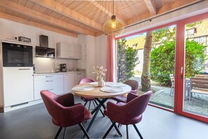 A modern kitchen with white cabinets, a built-in oven, and a dining area with a round table and red chairs.