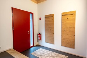 A hallway with a red door, a fire extinguisher, and two wooden panels on the wall.