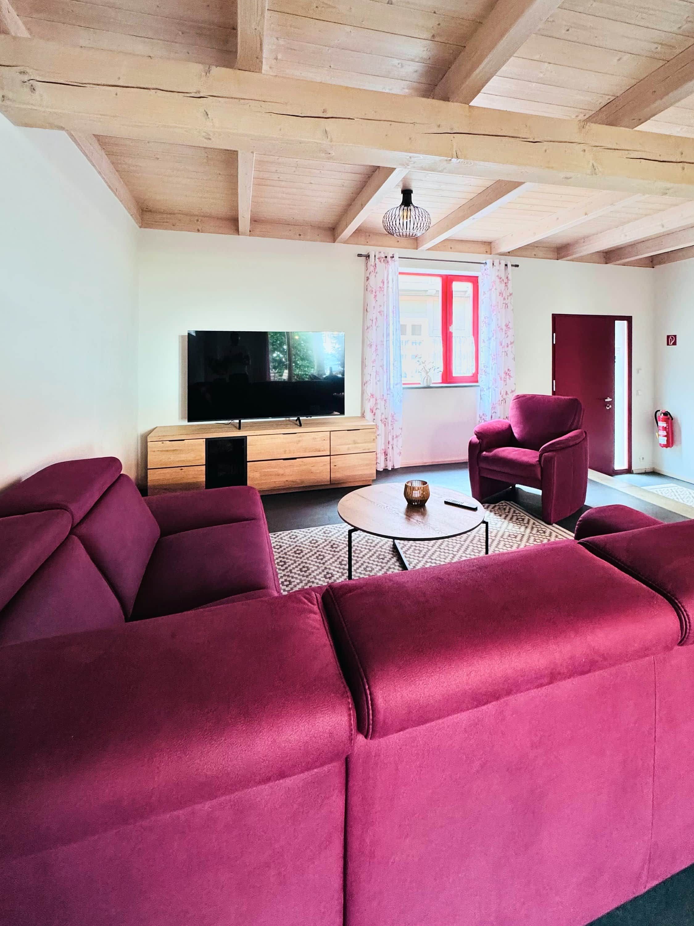 Een woonkamer met een houten plafond, een televisie, een bank, een stoel en een bijzettafeltje.