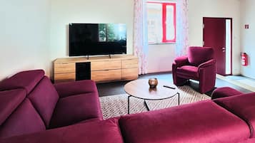 A living room with a wooden ceiling, a television, a sofa, a chair, and a small table.