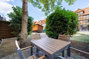 A wooden table and chairs in a garden area with a tree and a hedge.