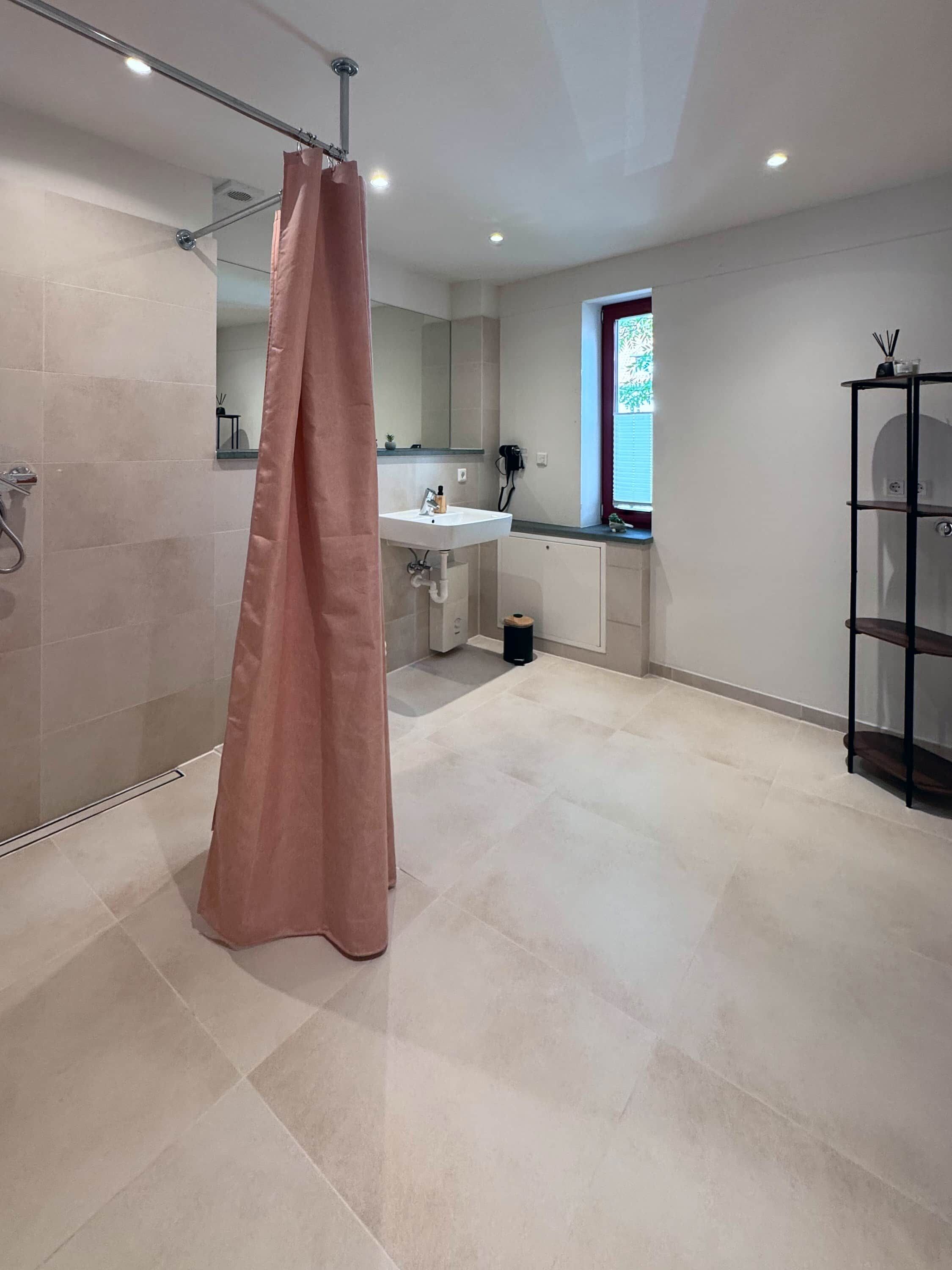Ein modernes Badezimmer mit Duschvorhang, Waschbecken und Fenster.