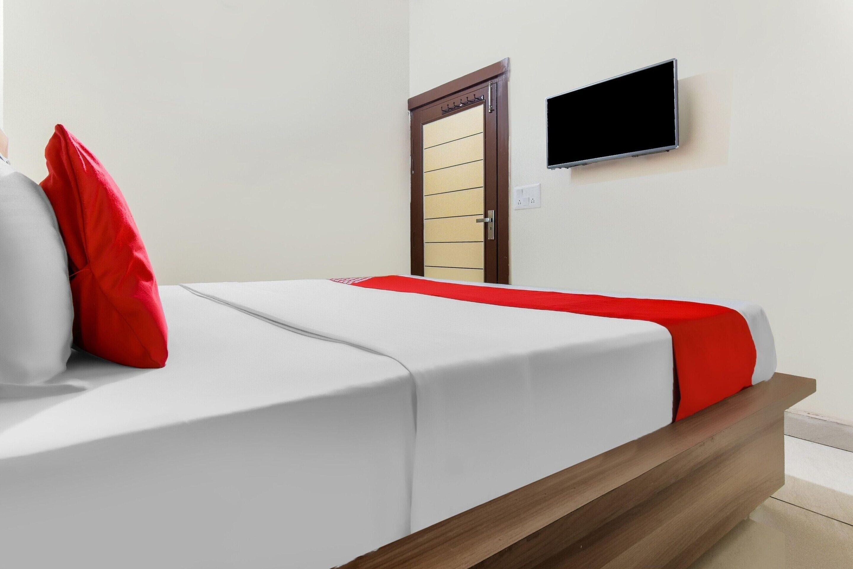 Una habitación de hotel con cama, televisor montado en la pared y puerta con manija.