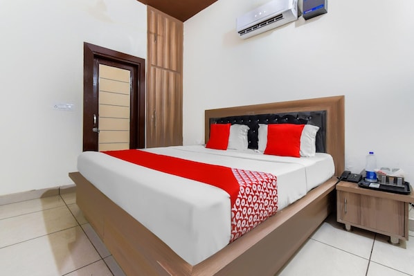 Una habitación de hotel con cama, mesita de noche, botella de agua y teléfono.