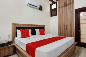 A hotel room with a bed, a wardrobe, a bedside table, and an air conditioning unit. - Classic Hotel Amigo (Thanesar)