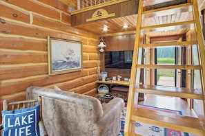 A log cabin interior with a wooden chair, a painting, a television, and a ladder. - Serene 1-bedroom Log Cabin - The St. Croix - on Lake Superior's South Shore (Port Wing)