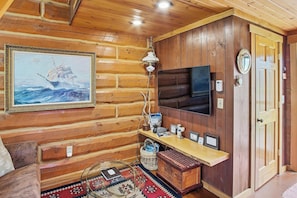 A log cabin interior with a mounted television, a framed painting, and a wooden shelf with various items. - Serene 1-bedroom Log Cabin - The St. Croix - on Lake Superior's South Shore (Port Wing)