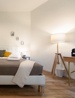 A neatly arranged hotel room with a bed, bedside table, lamp, and a small desk with a lamp. - Musart Green Room (Firenze)
