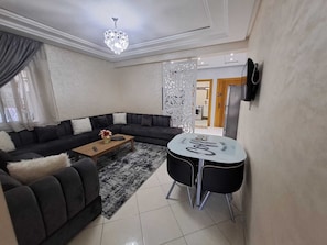 A modern living room with a sectional sofa, a coffee table, and a round table with chairs. - Lovely 2-bedroom apartment in Tanger near vibrant city spots (Tanger)