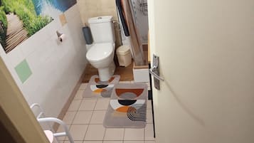 Un baño con inodoro, un bote pequeño para basura, zona de ducha y un perchero en la pared.