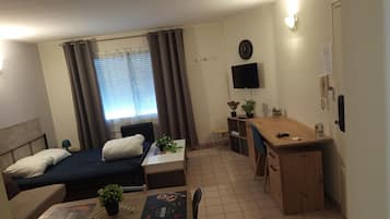 Habitación de hotel compacta con cama, escritorio, silla, televisor y ventana con cortinas.