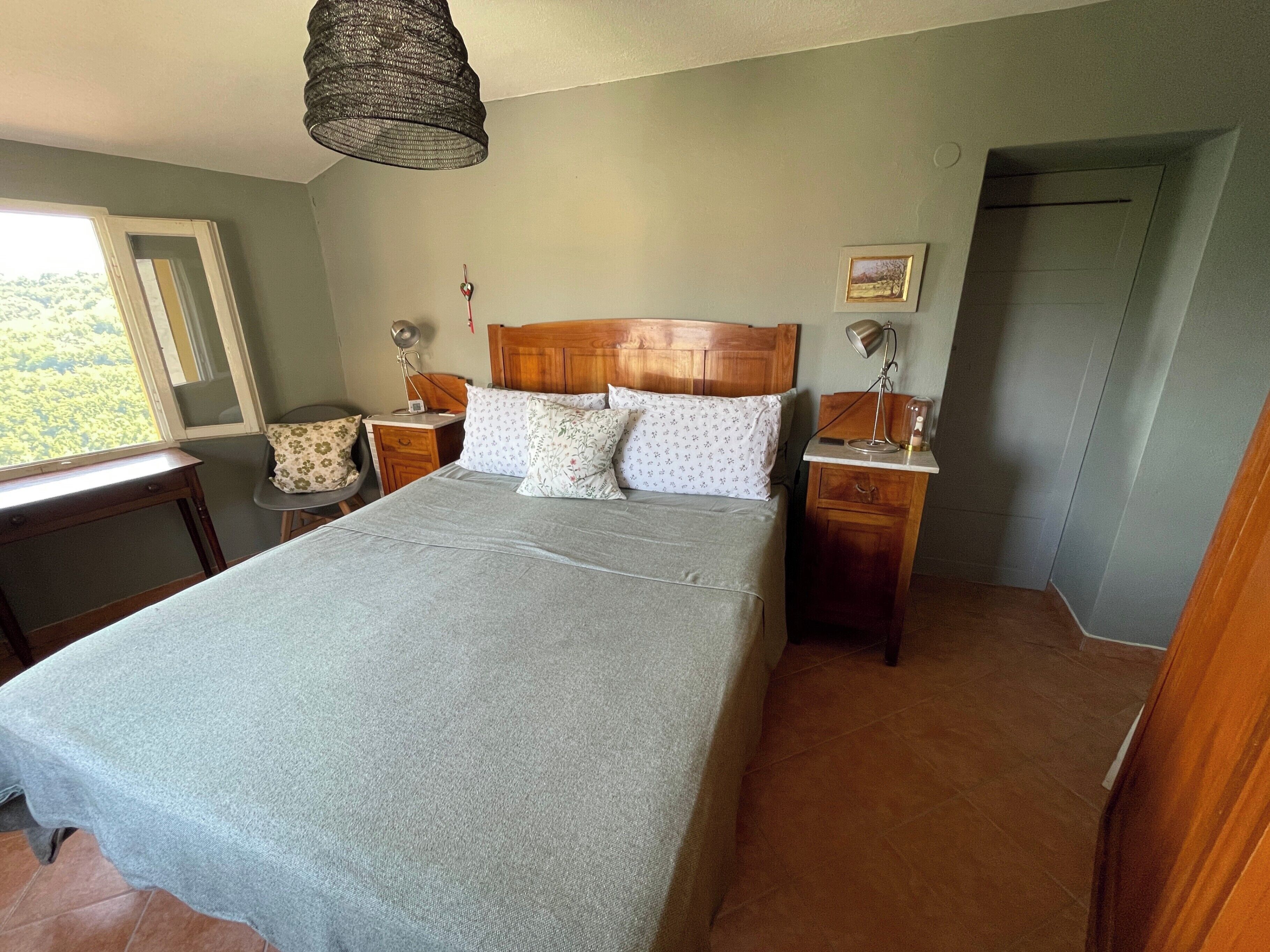 Une chambre à coucher avec un lit, des tables de chevet, une lampe, une chaise et une fenêtre.