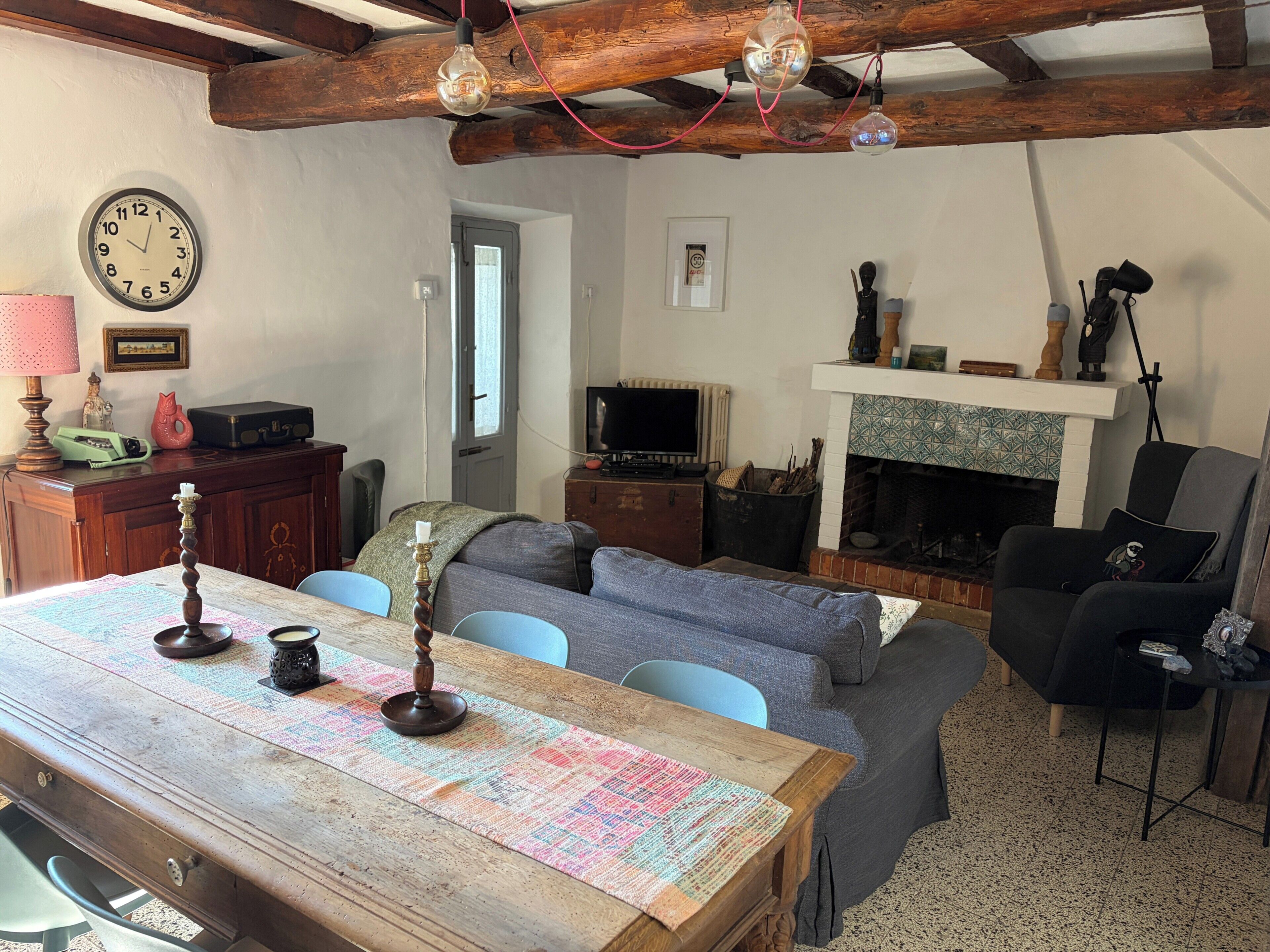 A cozy living room with a wooden table, a sofa, a fireplace, and a television.